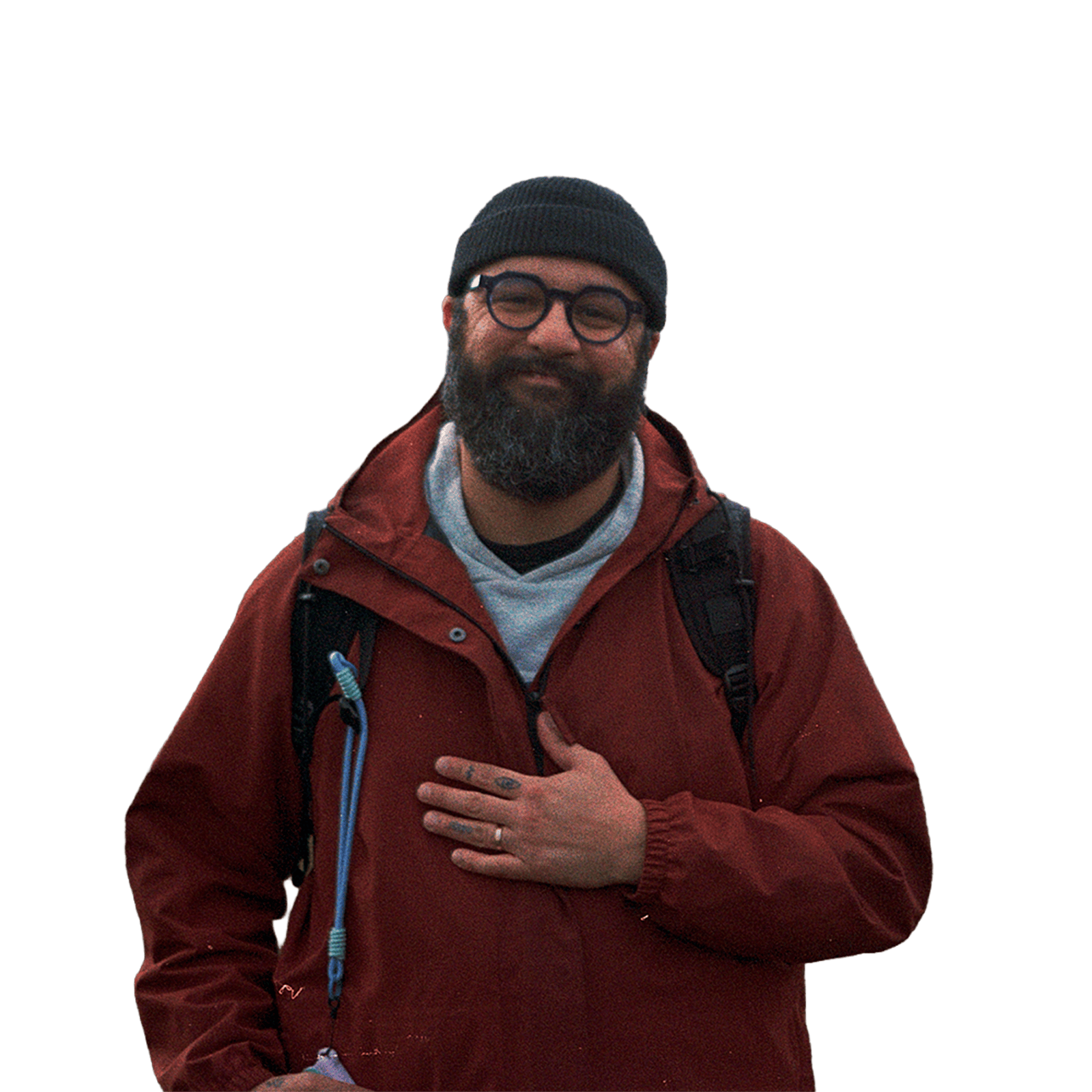 A film photograph of Noureddine from the waste up smiling while standing outdoors wearing a black beanie and a red rain coat.